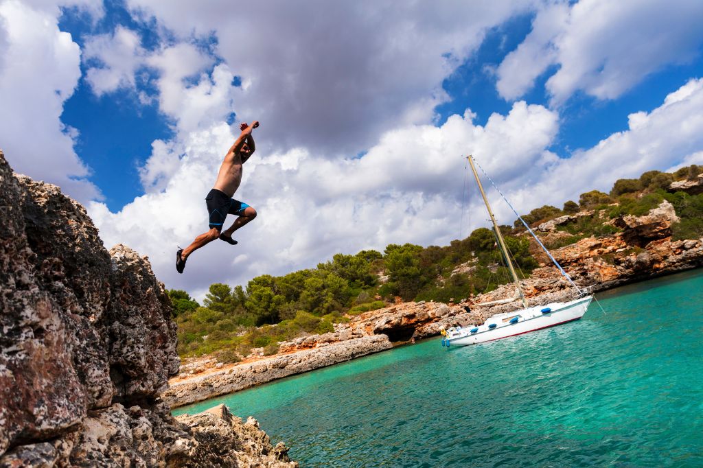 Mann springt von Klippen an der sonnigen Cala Sa Nau, Mallorca