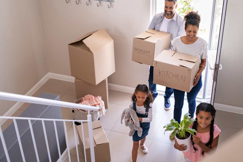 Eine Familie zieht in ein fertiges Haus, Eltern und Kinder bringen Kisten in das neue Haus