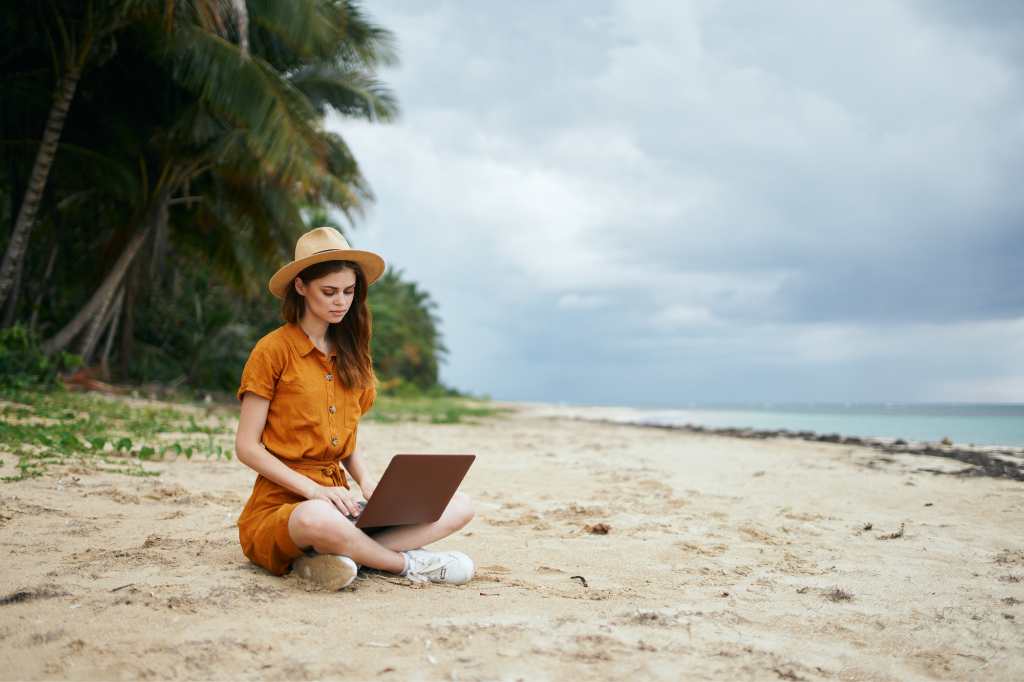 Remote-Arbeit - Mädchen arbeitet an einem Laptop am Meeresufer